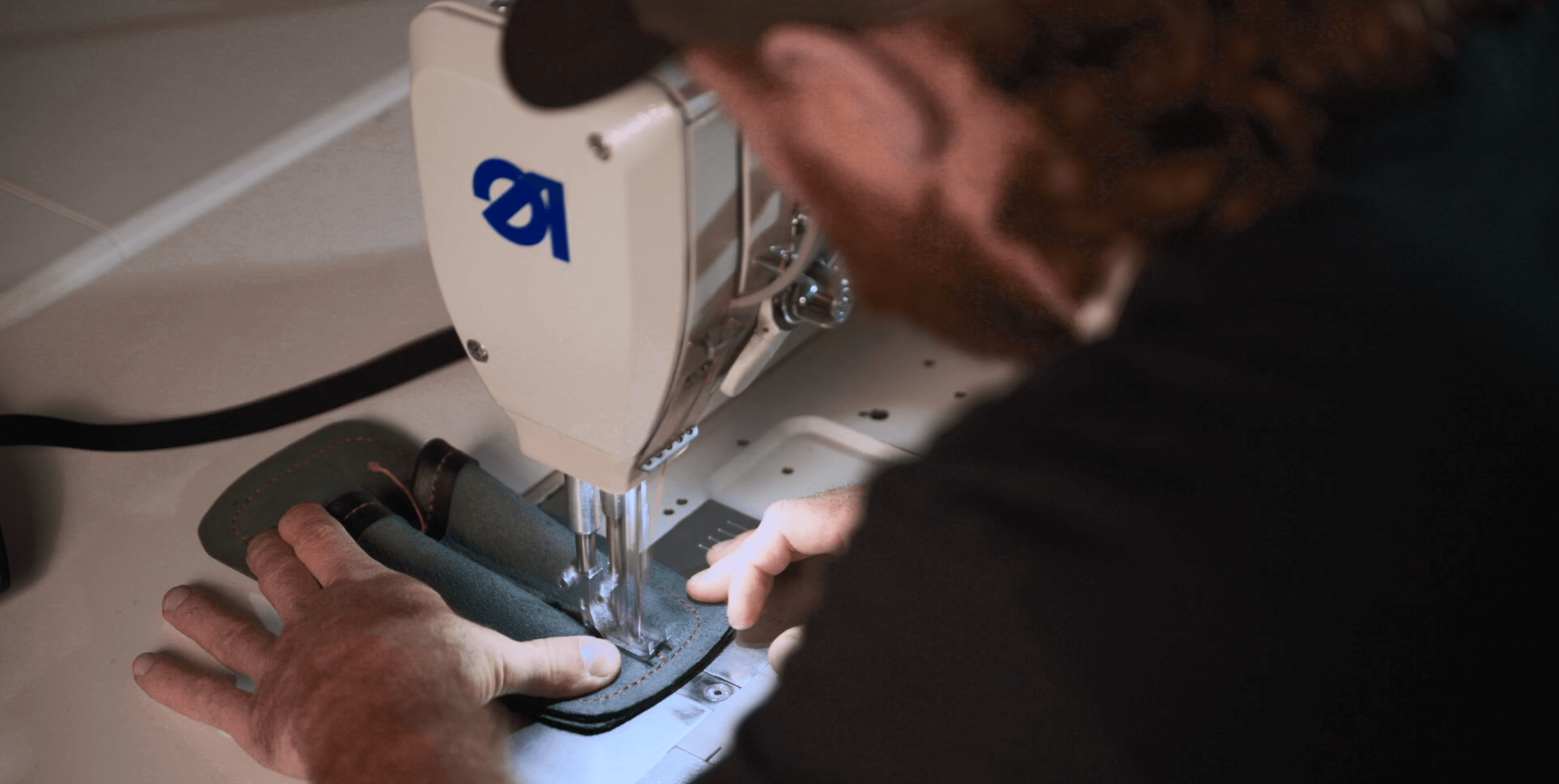 Close-up of a person using an industrial sewing machine to stitch leather, showcasing craftsmanship and skill.